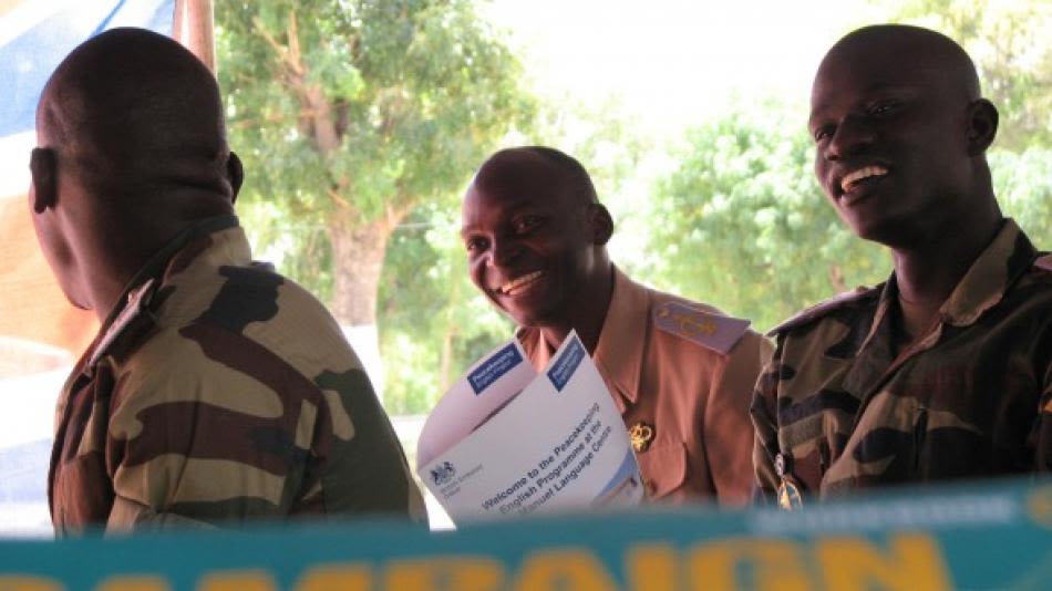 A man in a military uniform holding a Peacekeeping English Project leaflet.
