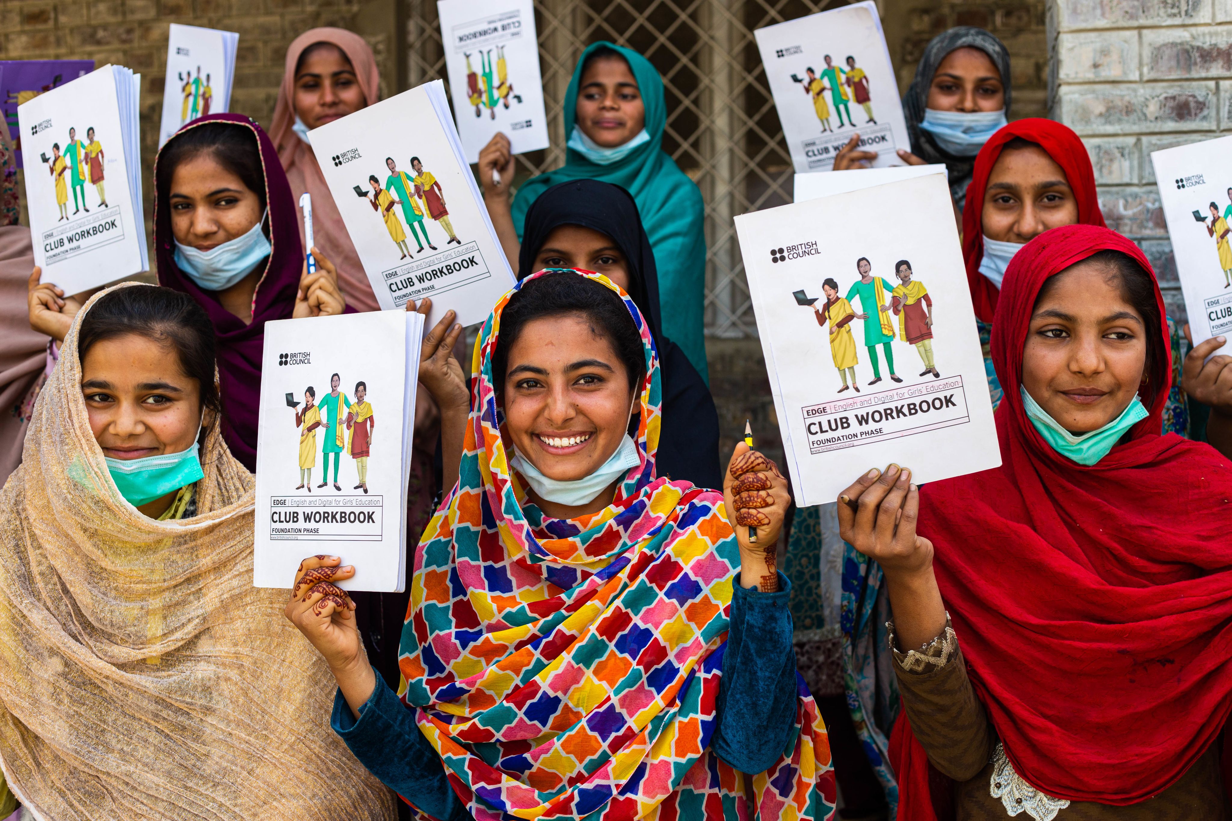 A group of smiling EDGE participants holding pens and pencils and their EDGE club workbooks.