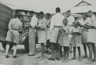 A group of adults and children reading while standing in front of a wagon full of books.