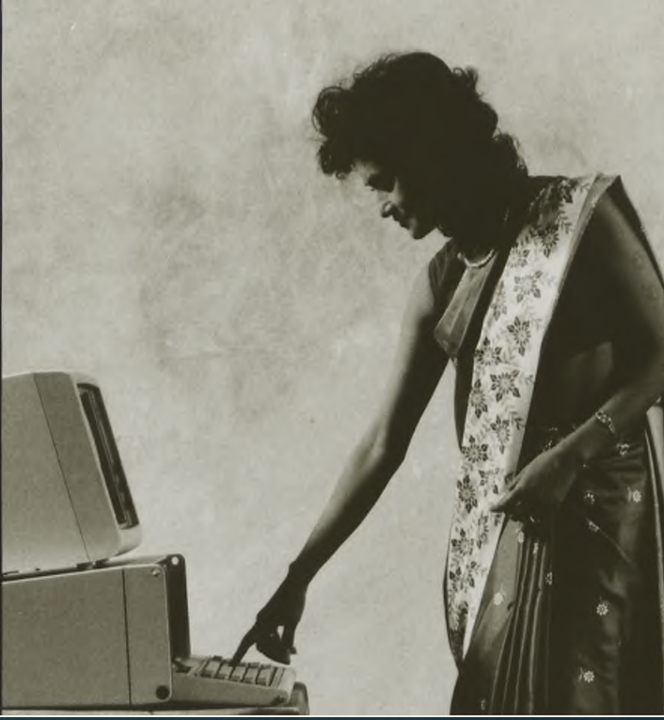 A woman pressing a computer key on a bulky desktop computer.