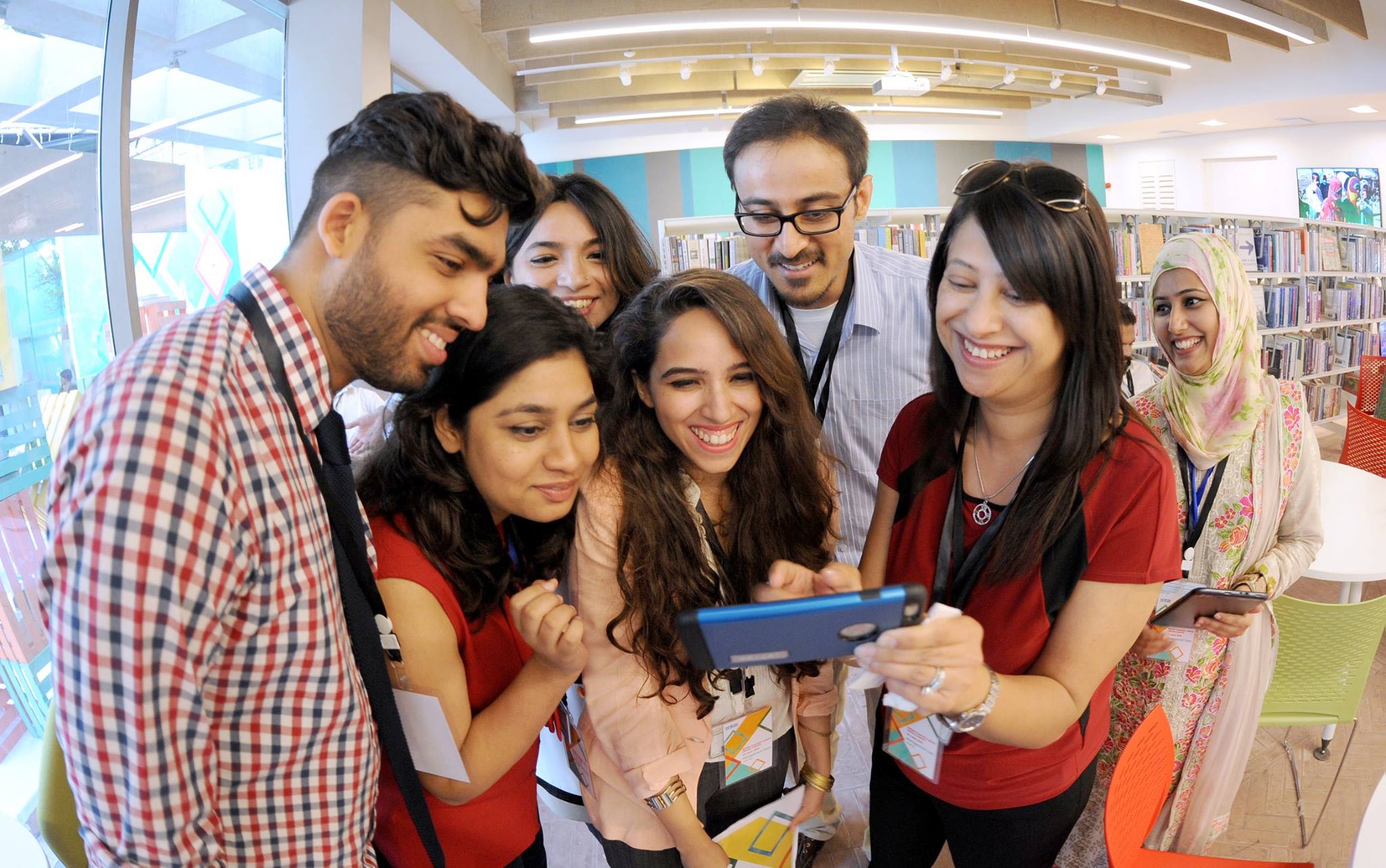 A group of smiling people looking at a mobile phone in a library.