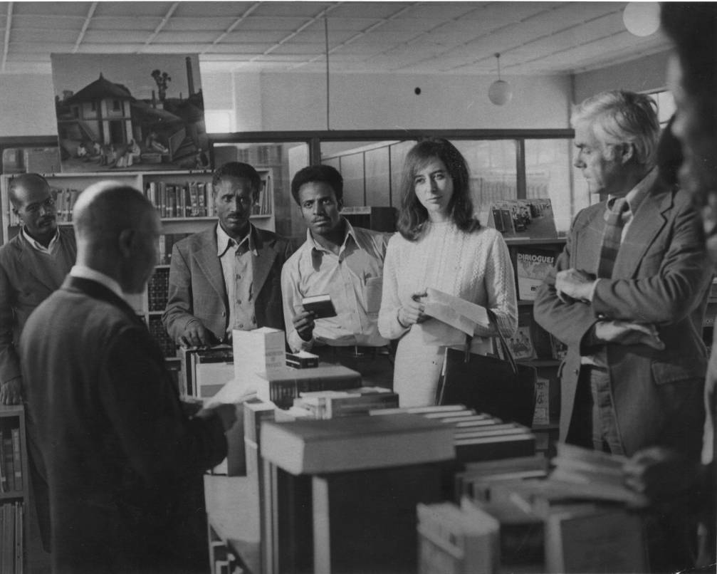 Four people in a library watch a man giving a presentation. 