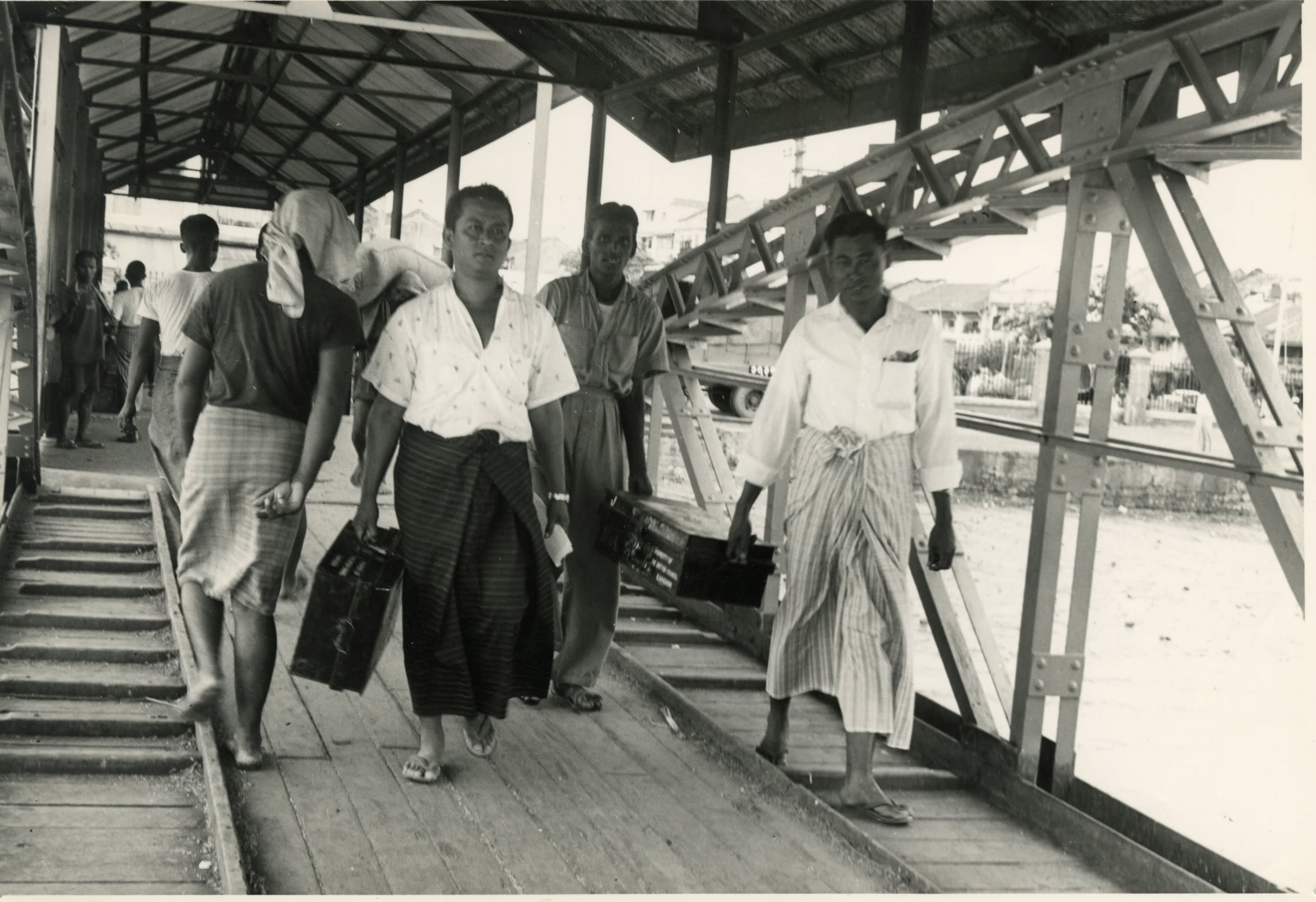 A group of people carrying large suitcases across a wooden bridge.