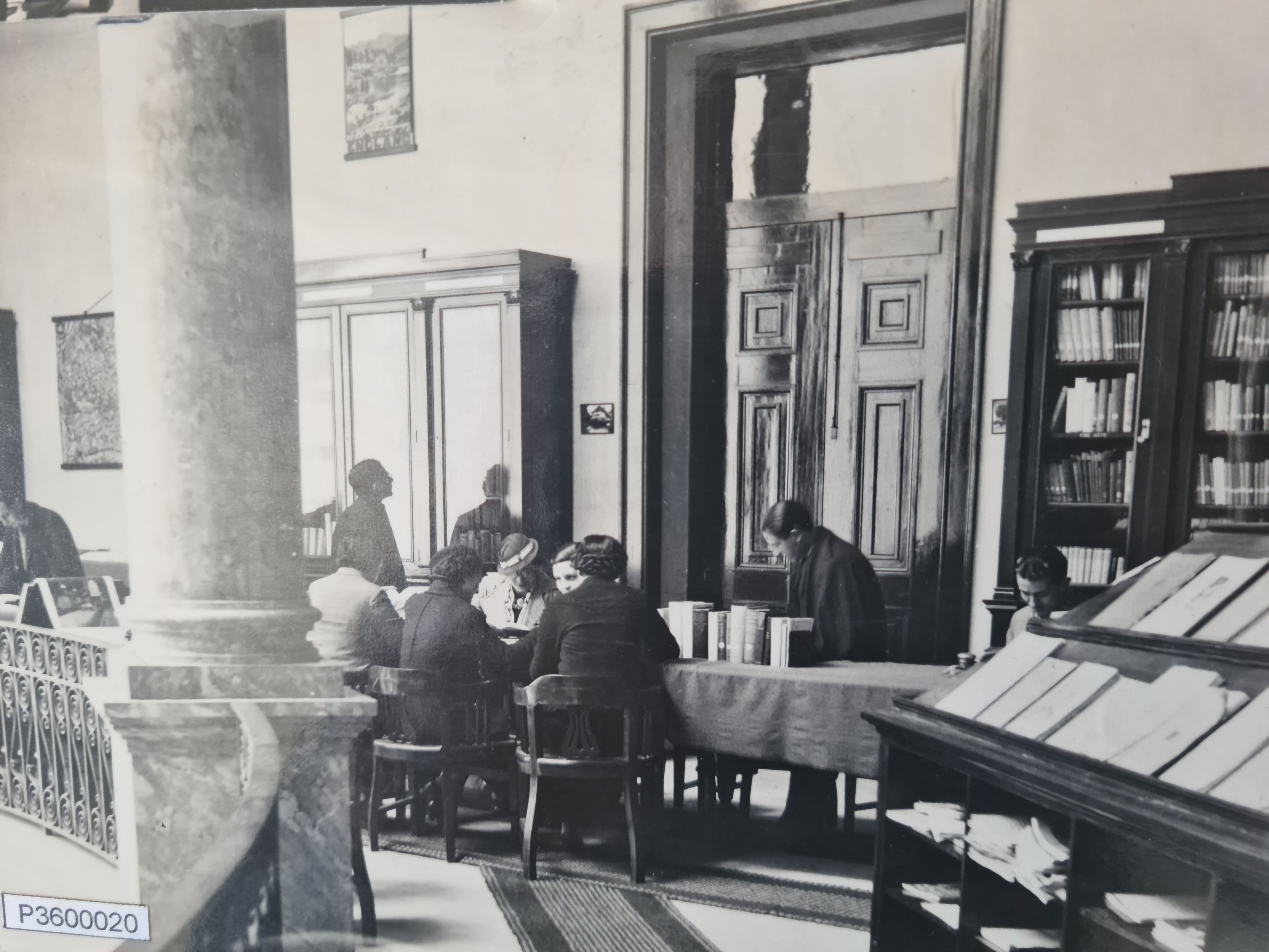 People reading and talking at a desk. Book cases and displays fill the room. 