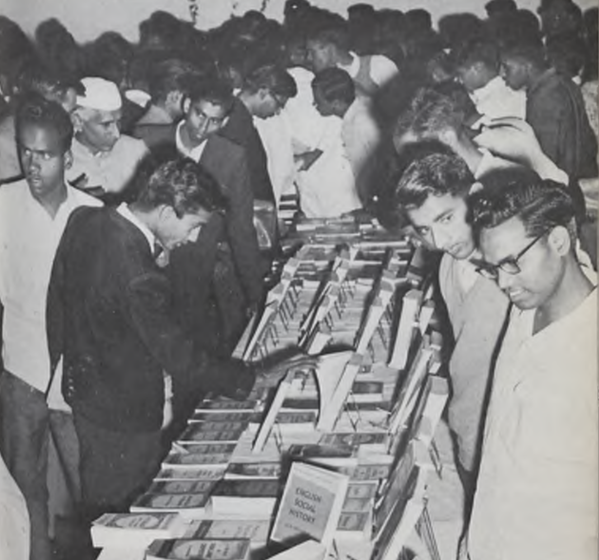 A crowd of men looking at a book display on a table. 