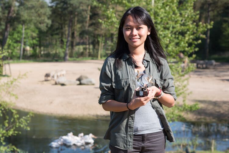 Trang holding an award in front of a wooded river.