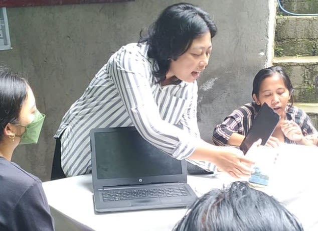 Ayu gesturing to a laptop with learners.